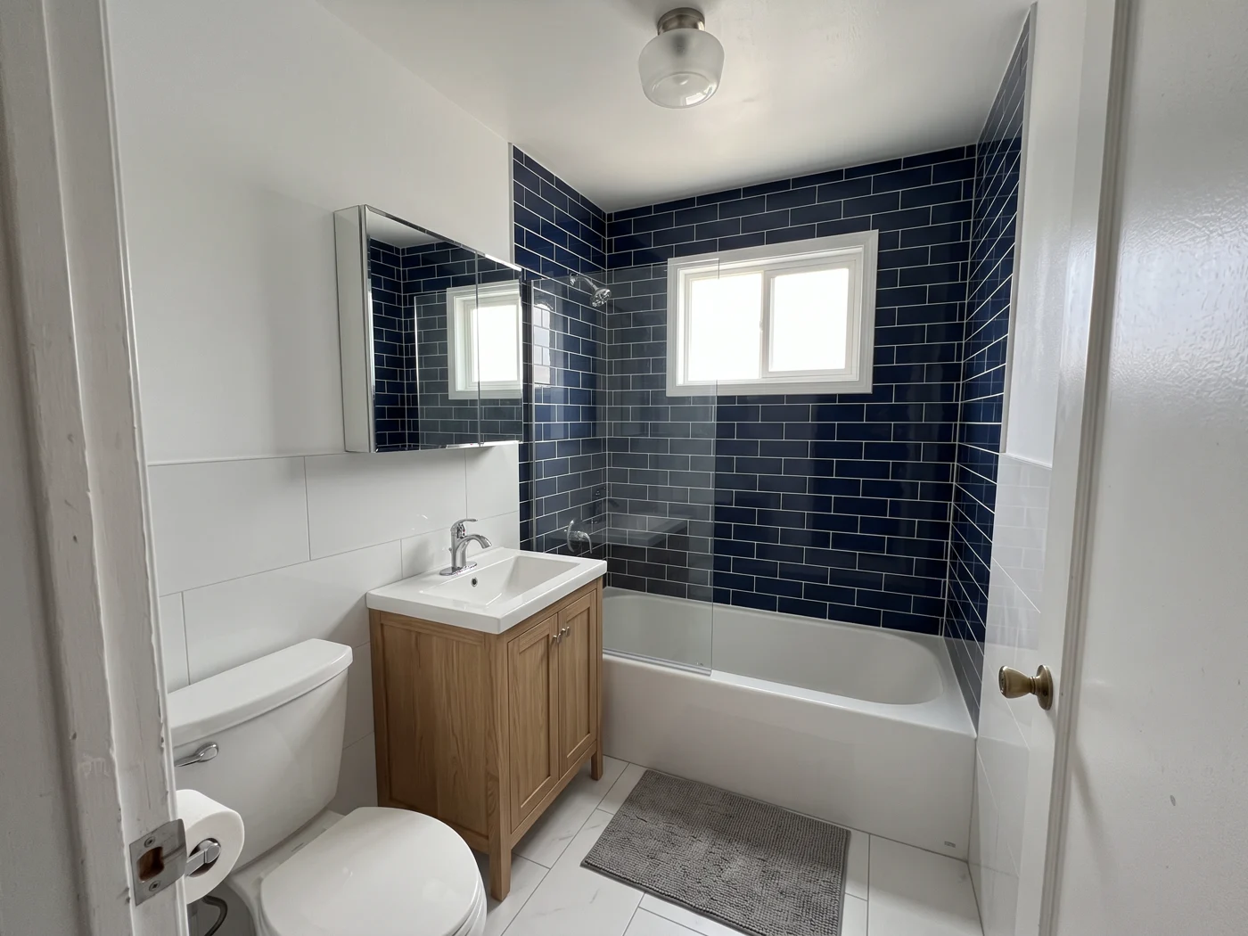 The finished bathroom with navy subway tile, glass shower panel and wood vanity