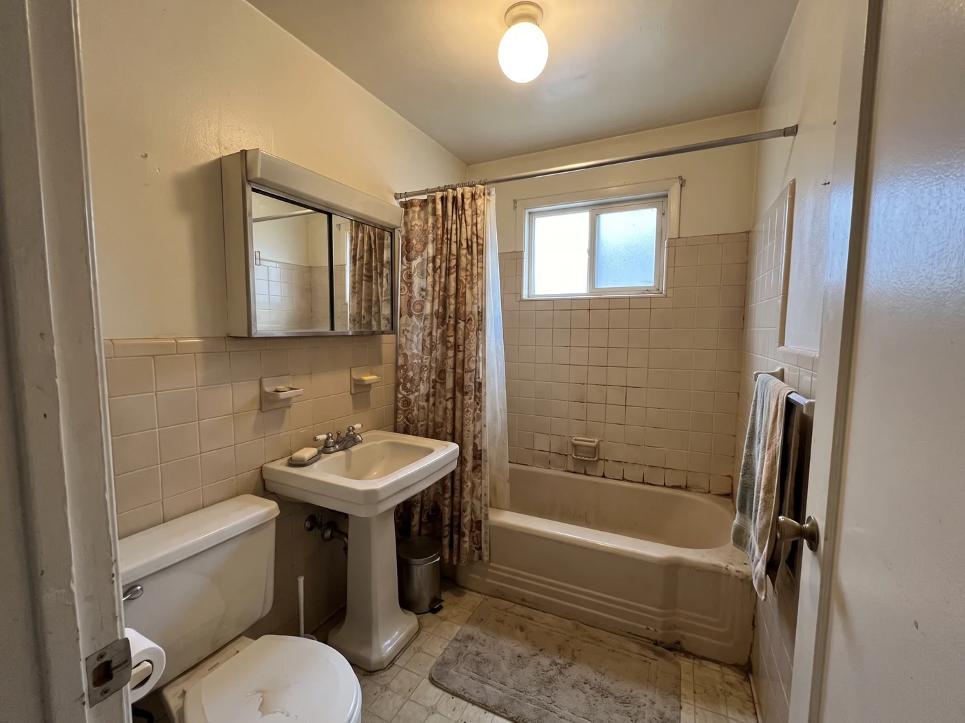 The same bathroom before the remodel, with worn beige tile and an old pedestal sink